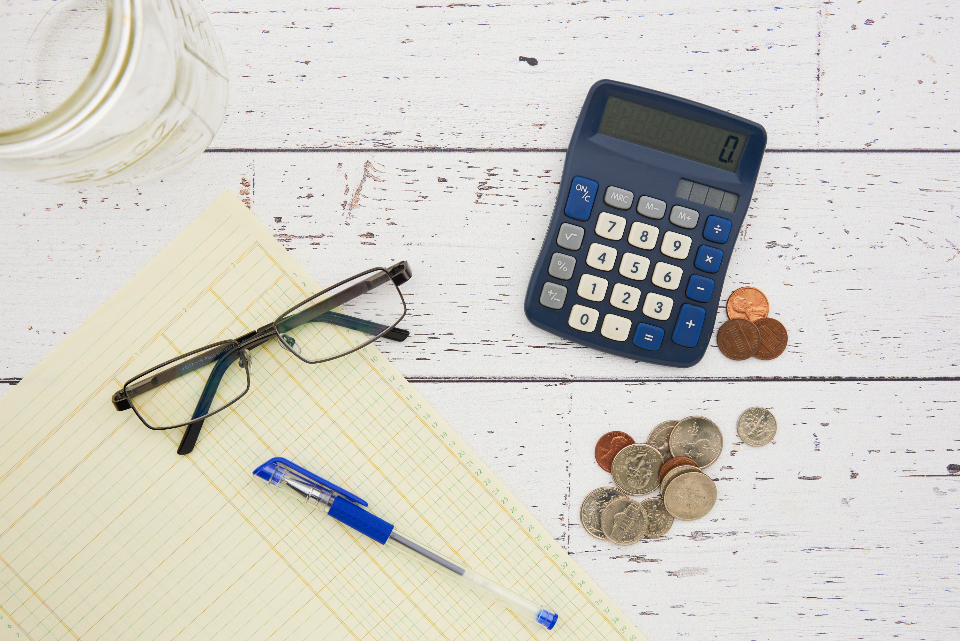 image of glasses, a calculator, legal pad, pen and coins