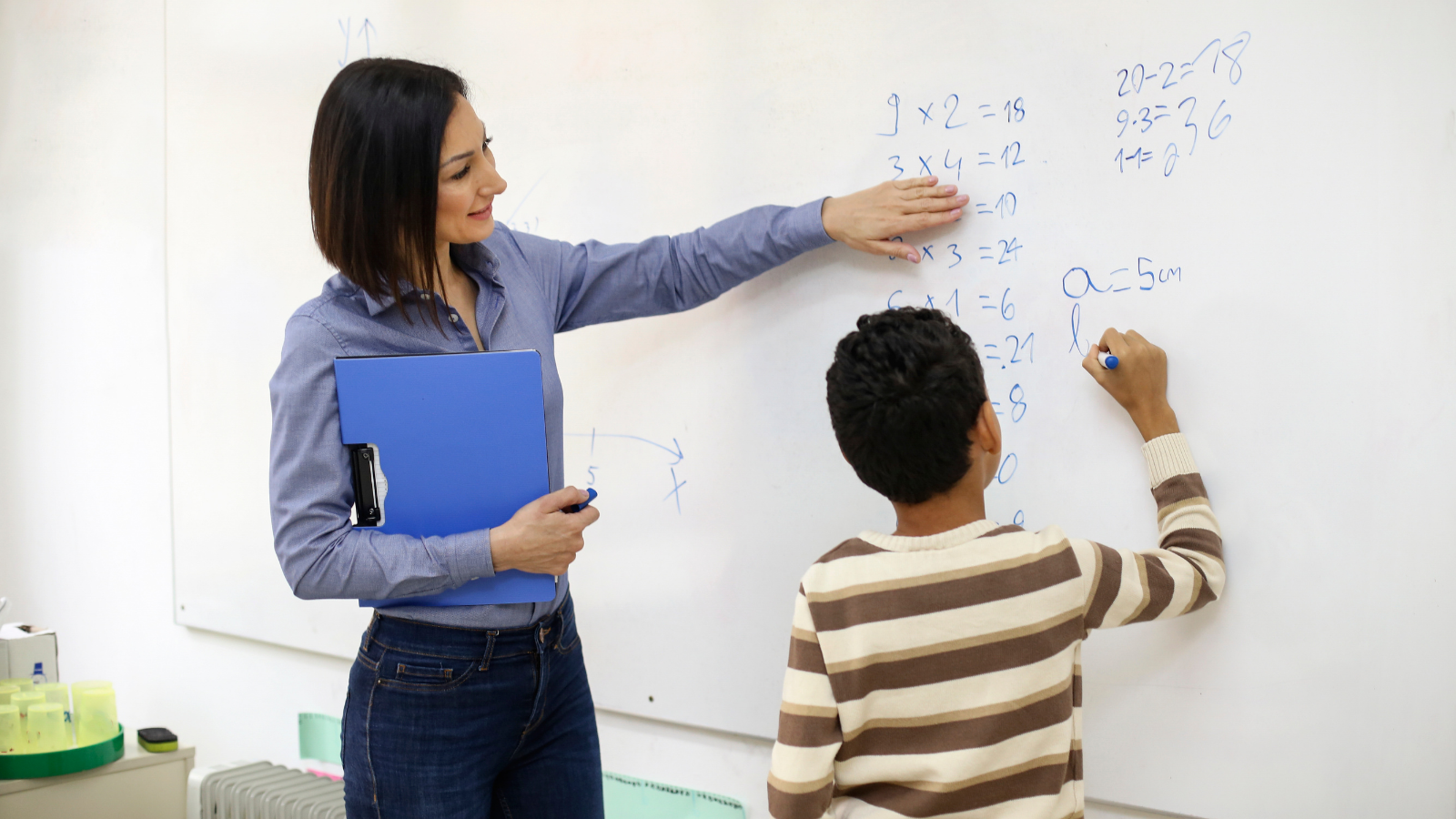 female teacher at whiteboard with young male student