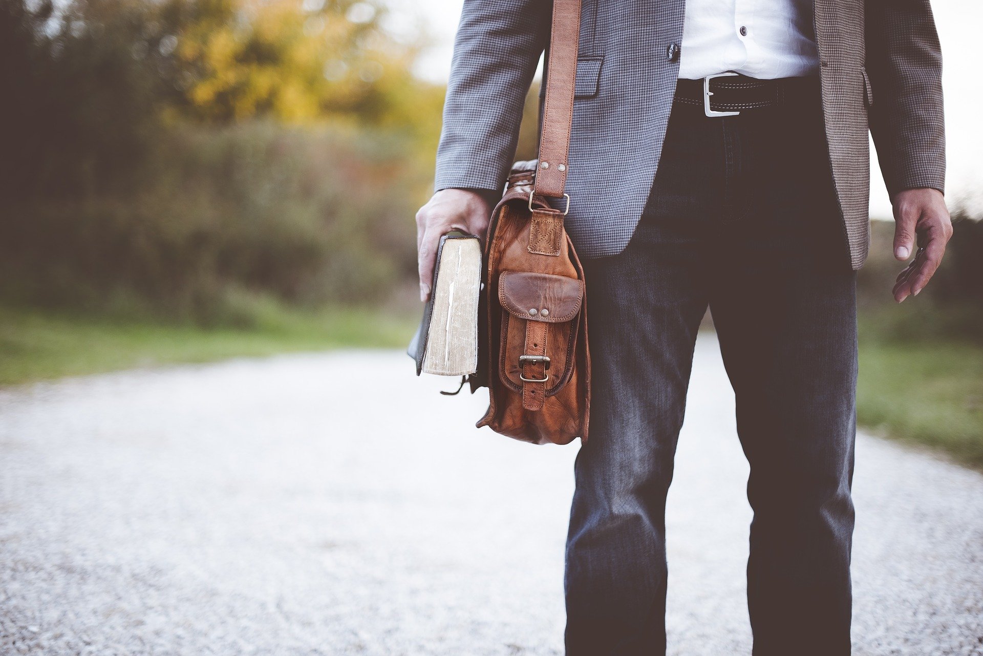 man with satchel holding a book