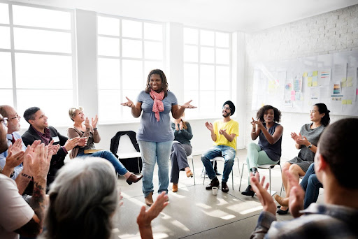 Group of diverse educators sitting in a circle of chairs with attention focused on a presenter in the middle