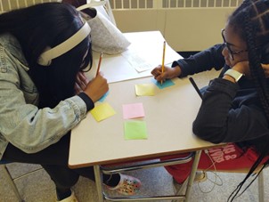 Students at a desk writing on post-it notes