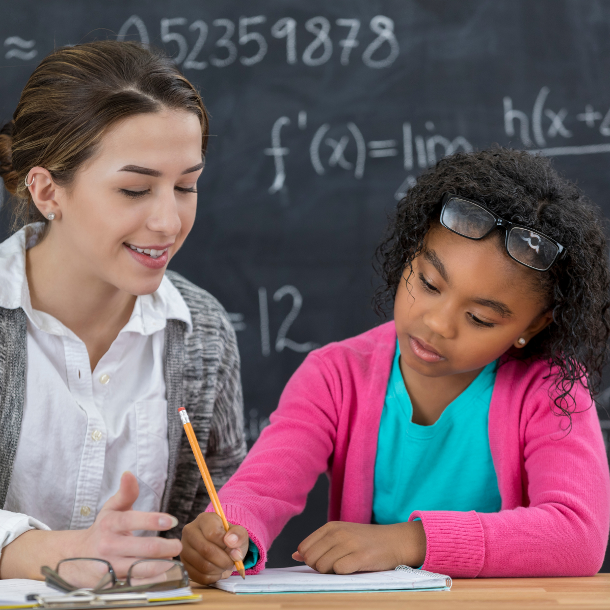 A female math teacher sitting at a table with a female middle school-aged student