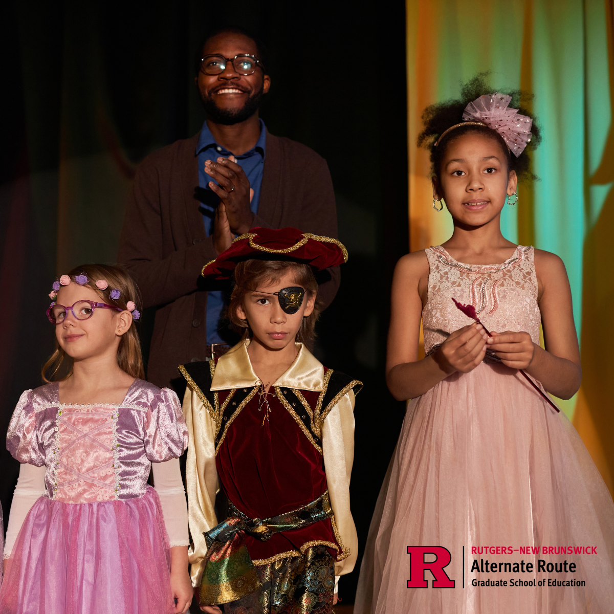 Male theater teacher standing onstage behind his students in their costumes
