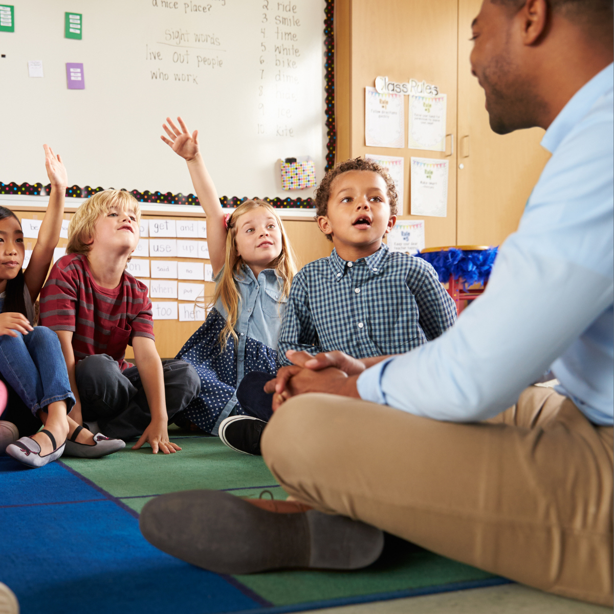 Male teacher sitting on the floor with his elementary students