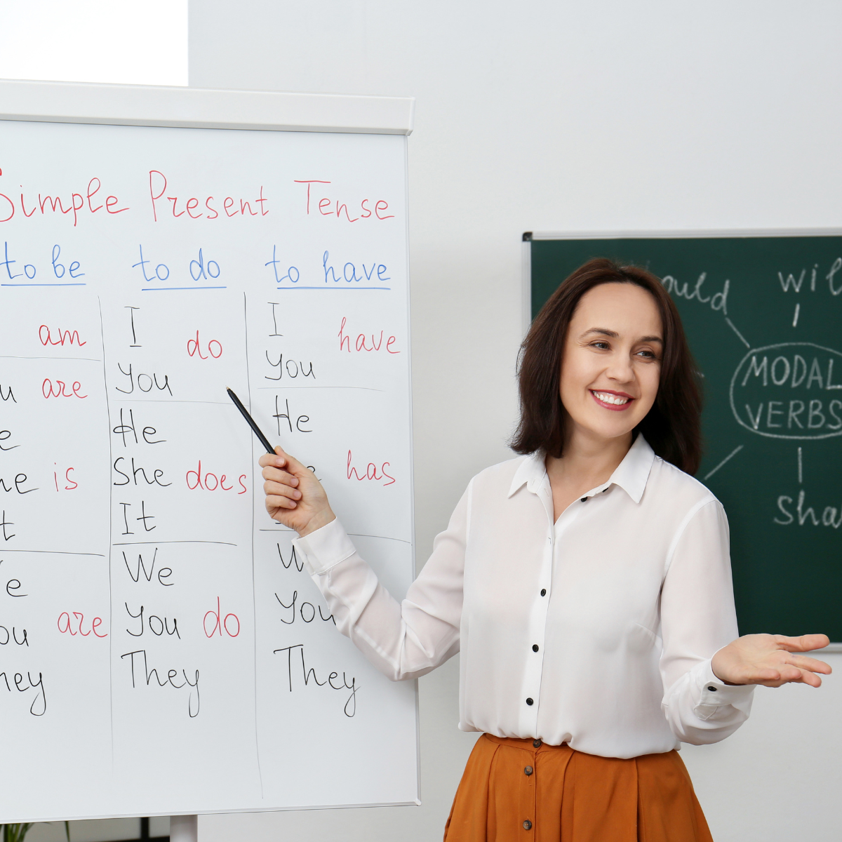Female teacher standing in front of a large pad of paper with word tenses listed