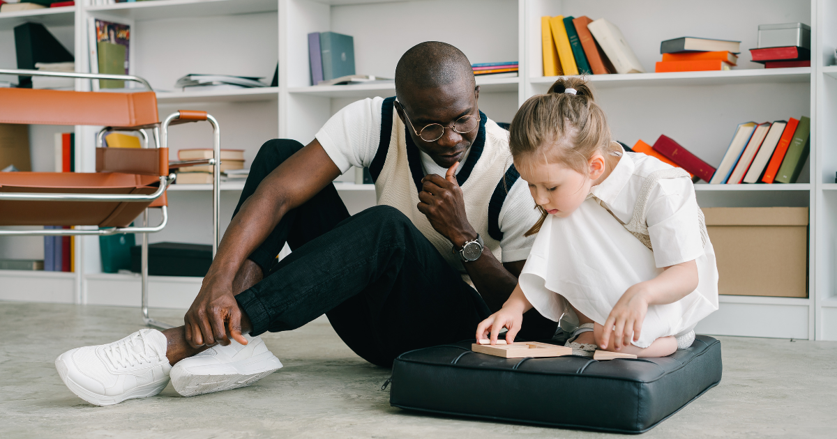 A male educator sitting on the floor with a young female 