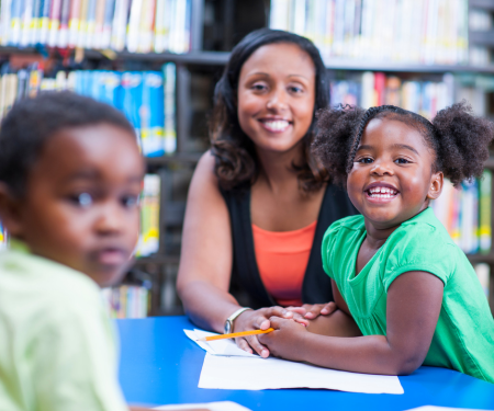 A woman with two children of color at a library table