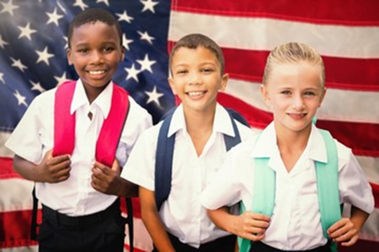Three diverse children wearing backpacks and standing in front of an American flag