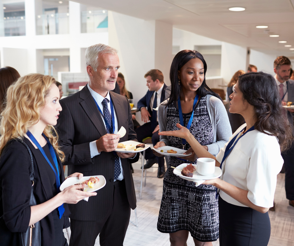 Three women and one man grouped around each other, holding breakfast plates at a conference