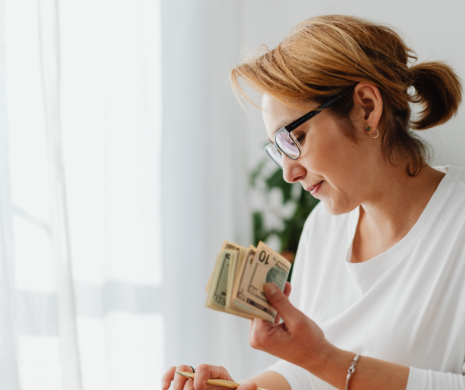 Woman holding money at a desk next to a window 