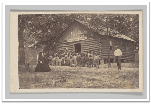 Group of Black students and their teachers standing outside a one-room schoolhouse