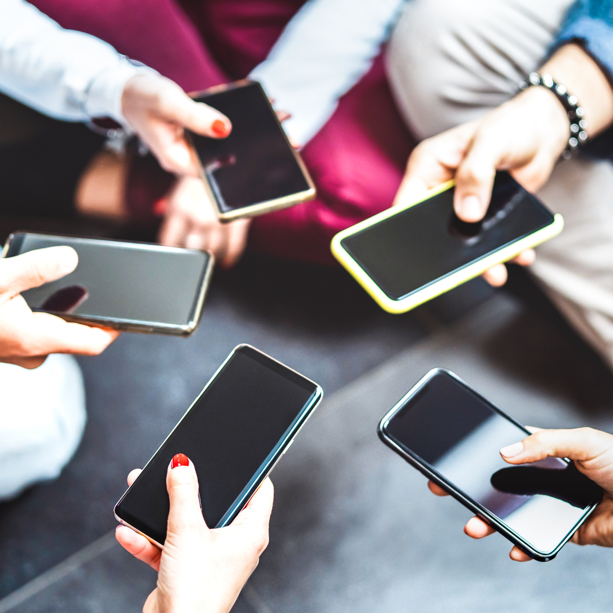 Group of students' arms holding smartphones in a circle