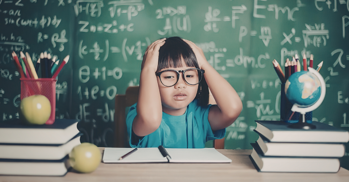 Elementary student with hands on her head, in front of a chalkboard filled with math problems