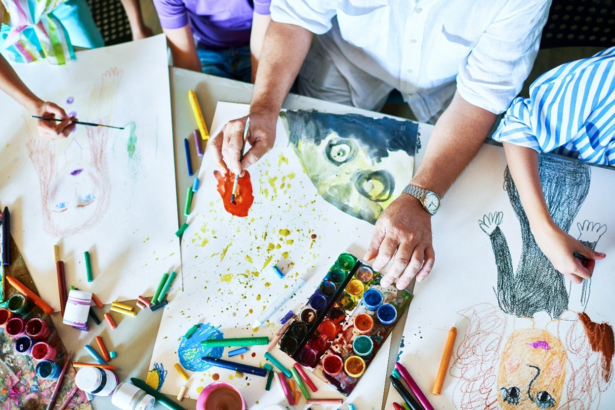 Table with art supplies with hands over three in-process art pieces