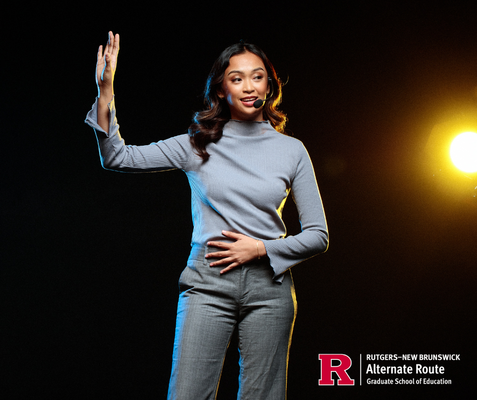 Woman with a wireless microphone standing onstage with her hand raised, engaging with the audience