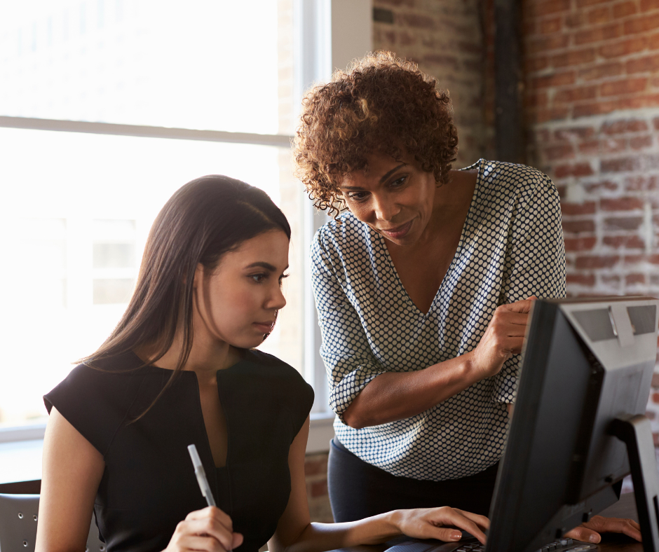 Woman at a computer being mentored by another woman standing next to her