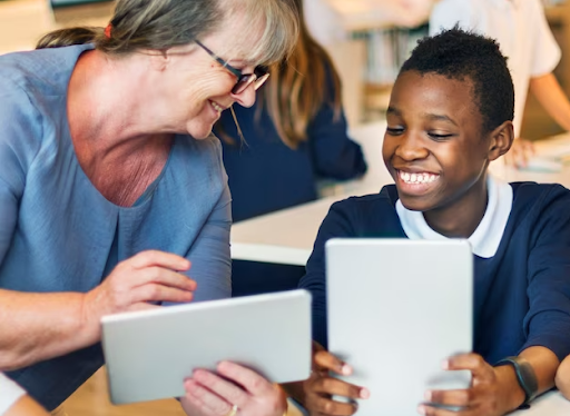 Woman at a desk with a student, holding tablets and smiling