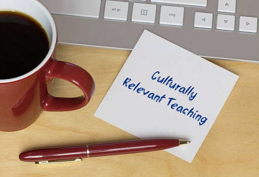 Desk with a keyboard, coffee cup, pen and note that says 'culturally relevant teaching'
