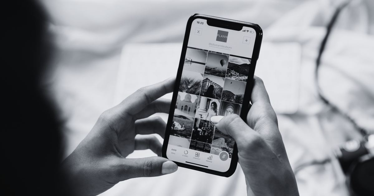 A black and white photo of a woman holding a phone while looking at a photo grid