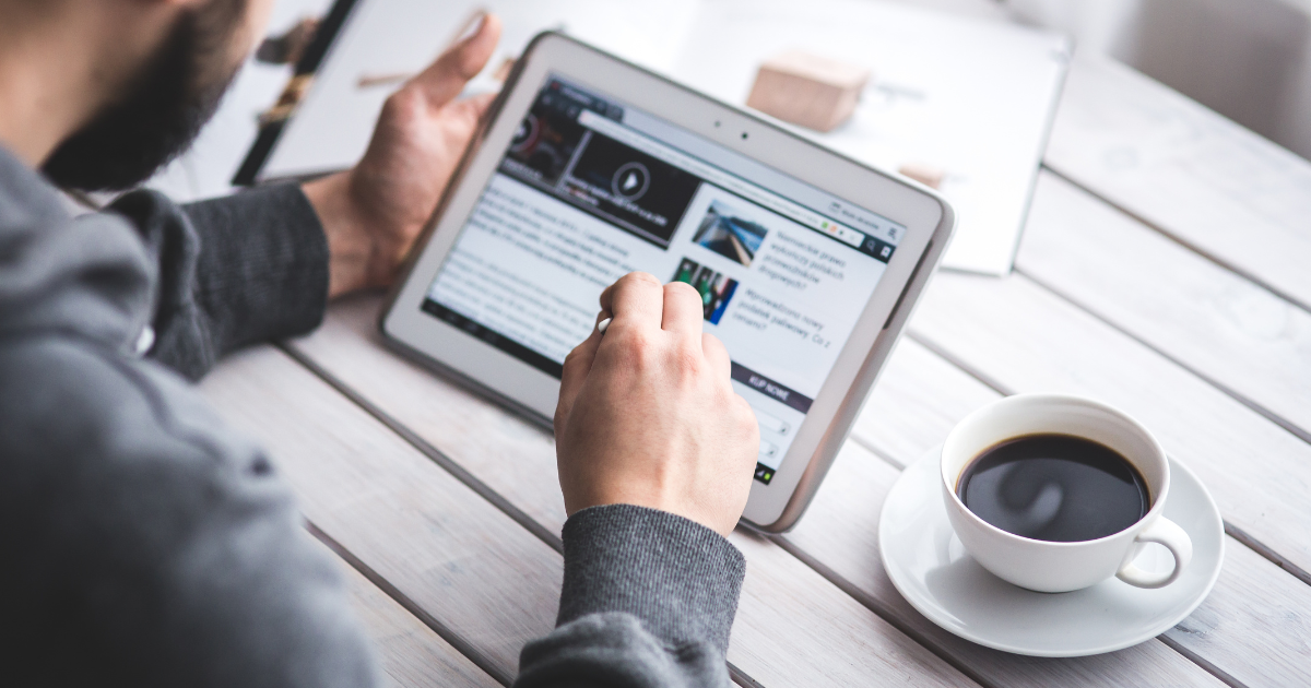 Man holding a tablet and reading a news article with a coffee mug to the right of him