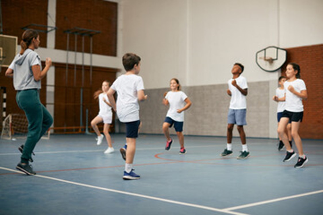 Students in a gym doing exercises led by a teacher