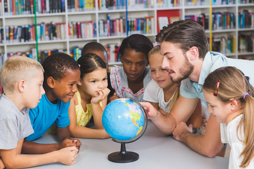 A diverse group of elementary students sitting around a globe with their teacher