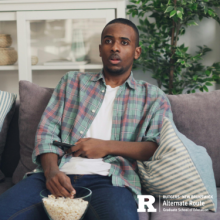 Man sitting on a couch, holding a remote with a bowl of popcorn on his lap