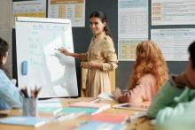 Woman in front of a table of students writing on a medium-sized whiteboard