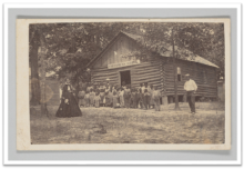 Group of Black students and their teachers standing outside a one-room schoolhouse