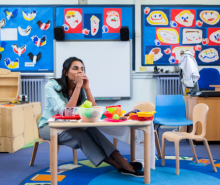 Female teacher sitting at a child's table, looking exhausted