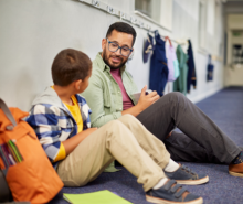 Male teacher sitting on the floor talking to an elementary school student