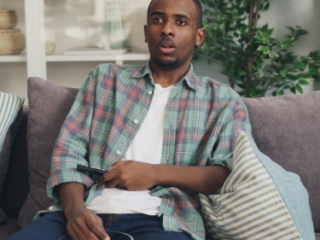 Man sitting on a couch, holding a remote with a bowl of popcorn on his lap