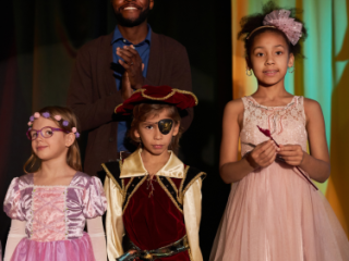 Male theater teacher standing onstage behind his students in their costumes