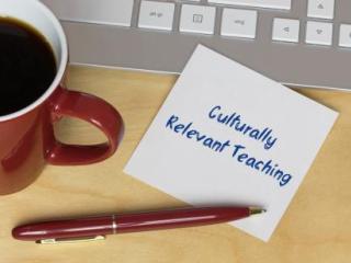Laptop, coffee mug, pen and a blank white card that reads "Culturally Relevant Teaching"