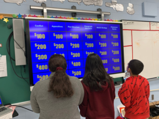 Students in a classroom with the Jeopardy board on a screen