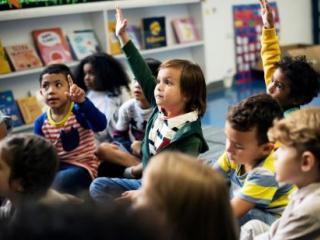 Group of elementary students sitting with hands raised