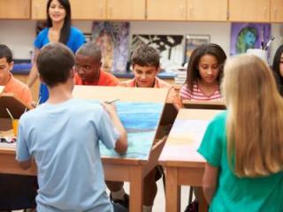 A group of diverse high school-aged students at a table working on a watercolor project