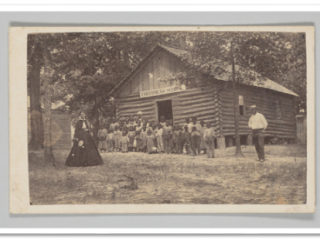 Group of Black students and their teachers standing outside a one-room schoolhouse