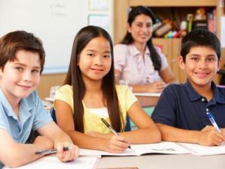 A group of multicultural students at a desk with their teacher behind, looking on happily