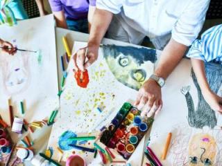 Table with art supplies with hands over three in-process art pieces