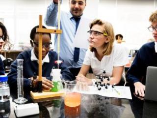 Group of science students around an experiment with their teacher overlooking