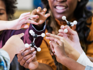 Teacher with a group of children's hands playing with a model of molecules