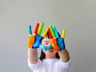 elementary-aged special education student holding up their hands, showing colorful paint on the palms