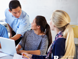 Male teachers helping two female support staff members at a desk