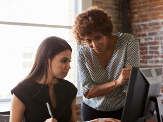 A woman in front of a computer with a woman mentor standing next to her