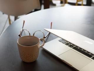 Image of a coffee mug and glasses next to a computer