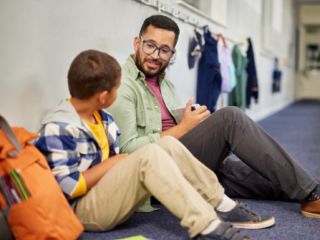 Male teacher sitting on the floor talking to an elementary school student