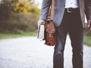 man with satchel holding a book