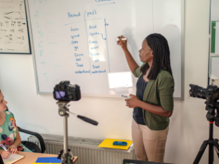 Two women in front of a chalkboard filming a class lesson