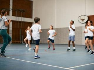 Students in a gym doing exercises led by a teacher